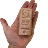 A hand holding a small copper ingot bar engraved with 'Cu', 'ONE KILO 9999 FINE COPPER', and 'MADE IN USA' on a plain white background.